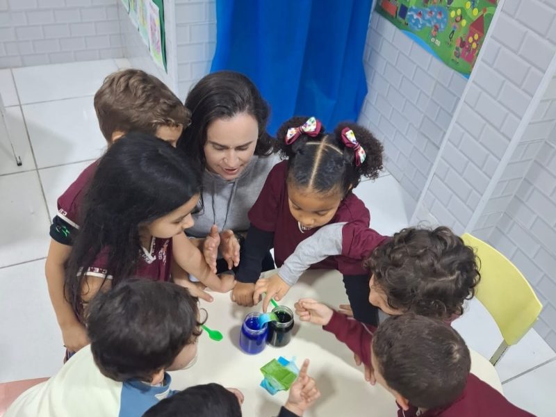 Professora e crianças do Pré I observando a experiência de capilaridade com água colorida
