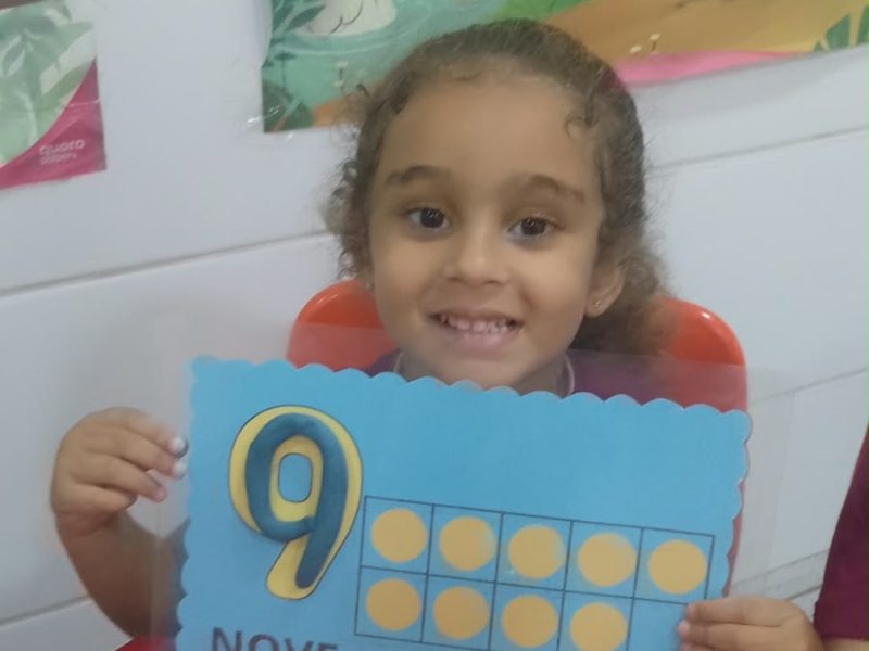 Menina sorrindo segurando a atividade com o número 9