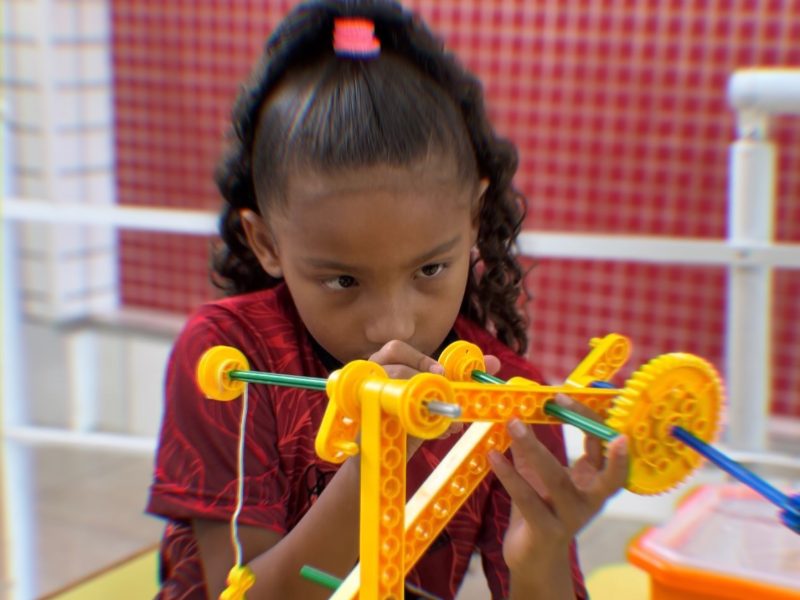 Menina montando uma estrutura com engrenagens na aula de robótica