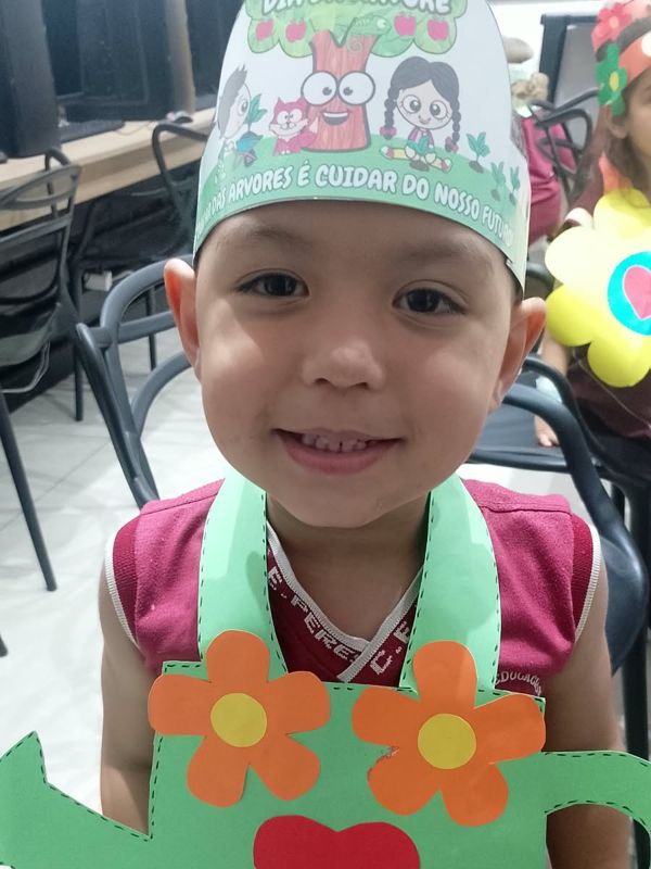 Menino sorrindo com chapéu e regador de papel da atividade de Primavera