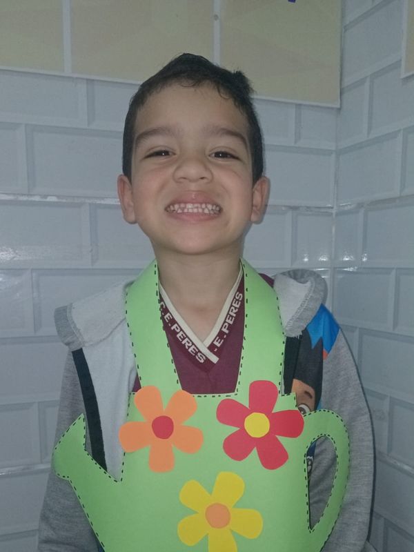 Aluno sorrindo com regador de flores de papel
