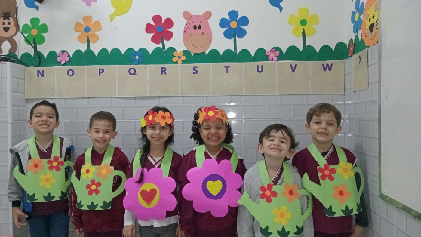 Alunos do Centro Educacional Peres sorrindo, com regadores e flores de papel feitos na atividade de Primavera